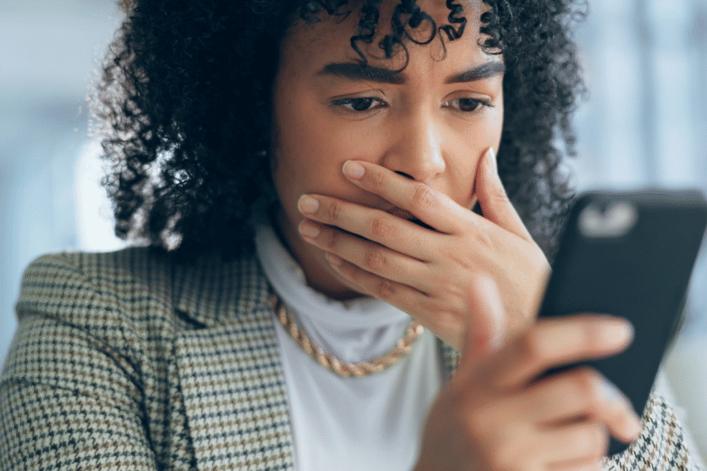 A concerned woman holding a smartphone, reacting to warning signs of a scam web development agency before making a payment.