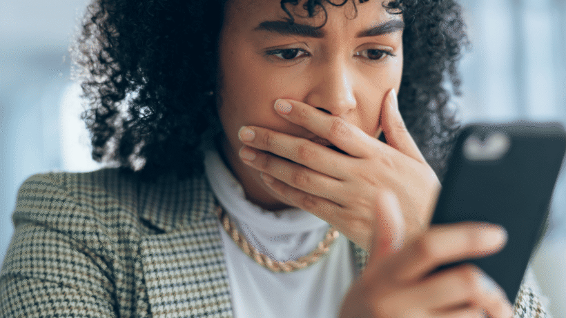 A concerned woman holding a smartphone, reacting to warning signs of a scam web development agency before making a payment.